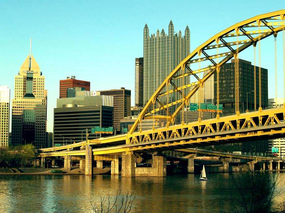 a yellow bridge spans a wide river, a glass castle rises above other buildings in the background
