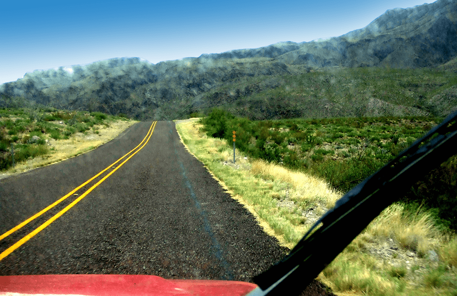 the sliver of a hood of a red Jeep Wrangler, a road drives well of into the desert mountain