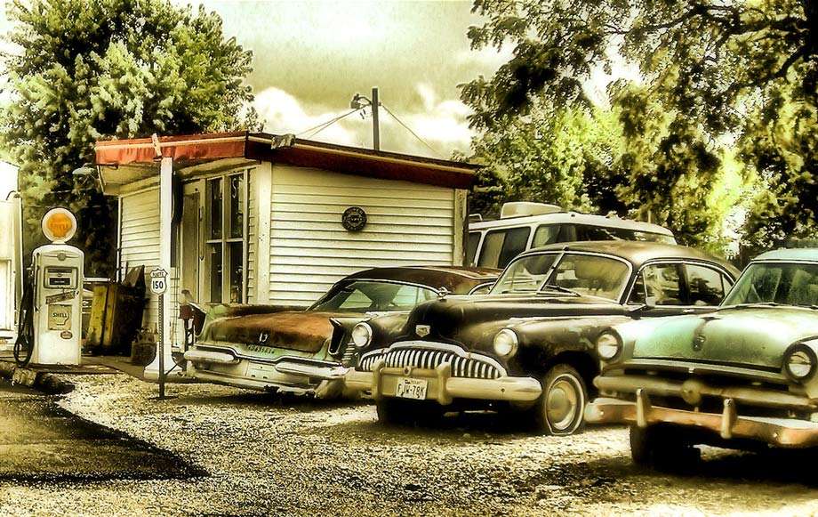 vintage cars outside of a gas station in some beautiful wooded locale