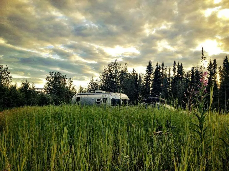 a silver Airstream peeks just over a field of grass