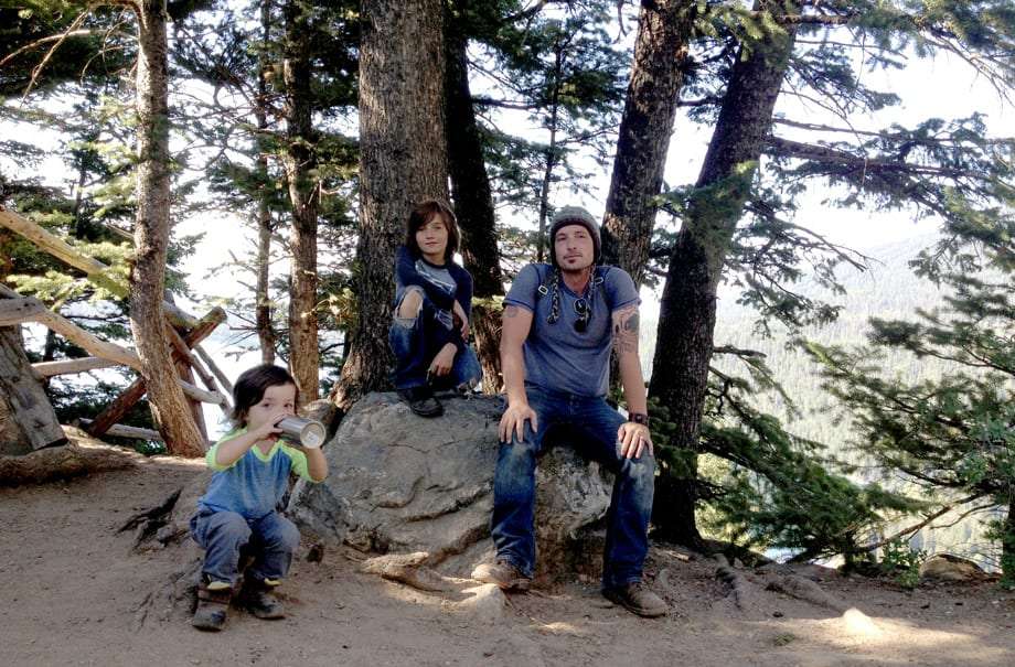 a dad and two of his boys rest at the top of a mountain