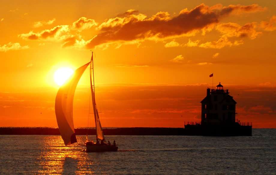 silhouette of a sailboat and a lighthouse against a brilliant burnt orange sky