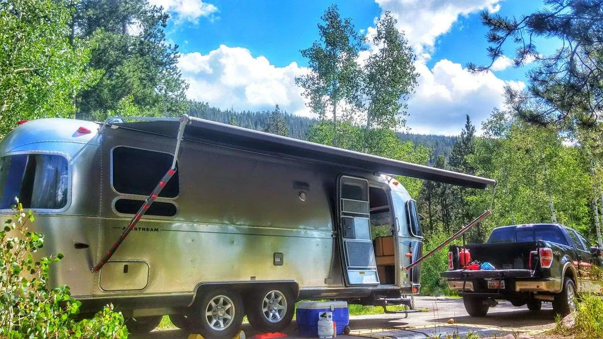 a beautiful silver travel trailer reflects the forest around