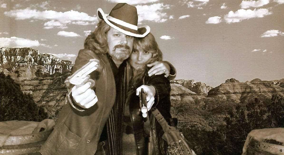 Jenn and Greg dressed up like wild west outlaws against a backdrop resembling the mountains of Utah