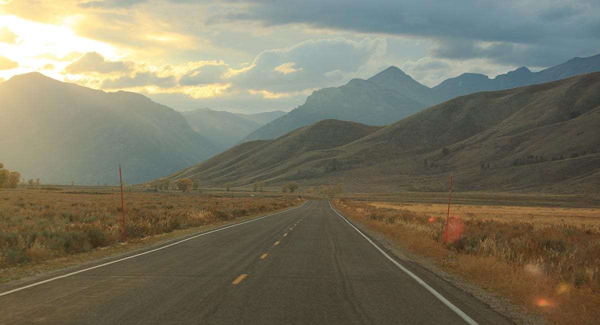 a road triangles into the horizon, mountains and the sunshine of a new promise all that the distance holds