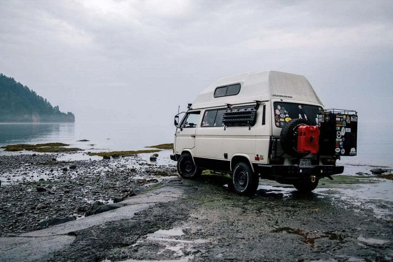 a white vanagon with a high top and a bunch of gear on the back, in a rather kick ass setting if i do say so myself
