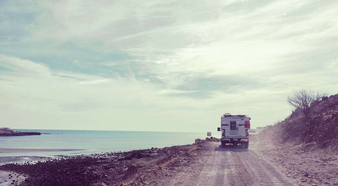 a Ford F-350 with a Four Wheel Drive truck camper (belonging to the Mali Mish family) drives down a dirt road in Mexico's Baja Peninsula