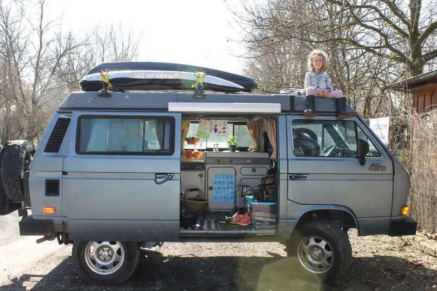 a gun metal blue vanagon with a young girl sitting on the roof, door open