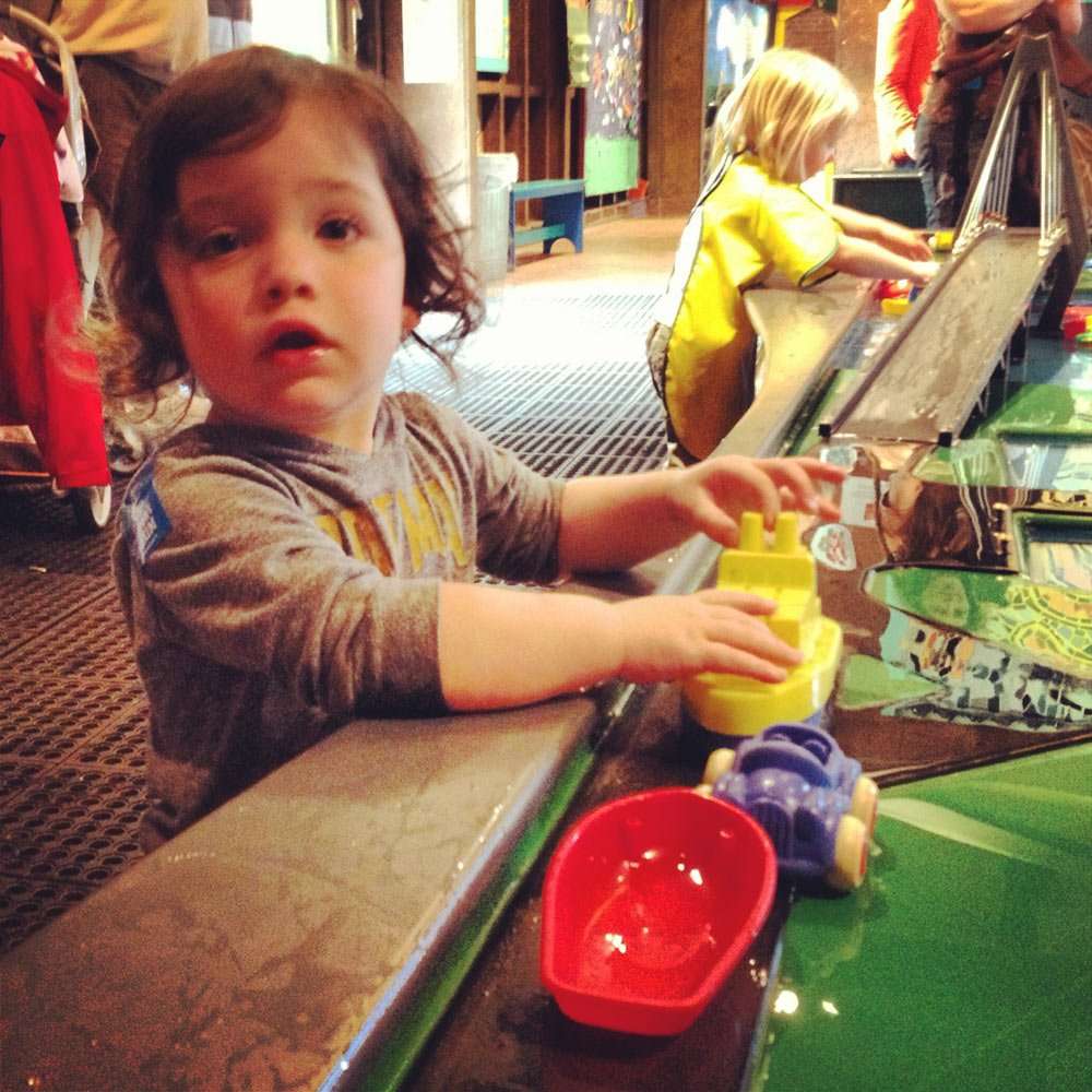 a young boy plays in a river at a museum