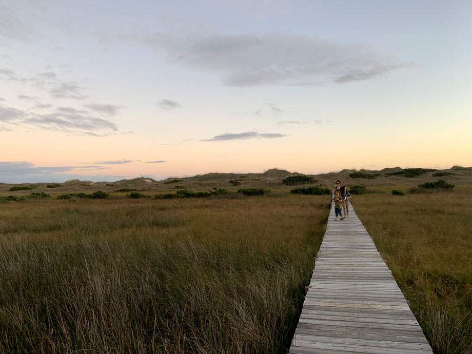 a family walks along a boardwalk through marshlands to from the dunes and beach in Cape Hatteras National Seashore