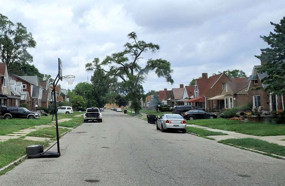 a street with brick homes, trees and a basketball hoop