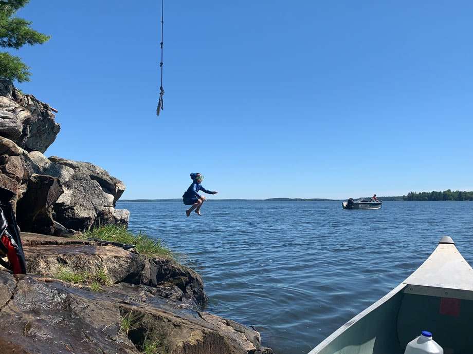 a boy jumps into a lake from a rope swing and off of a small cliff