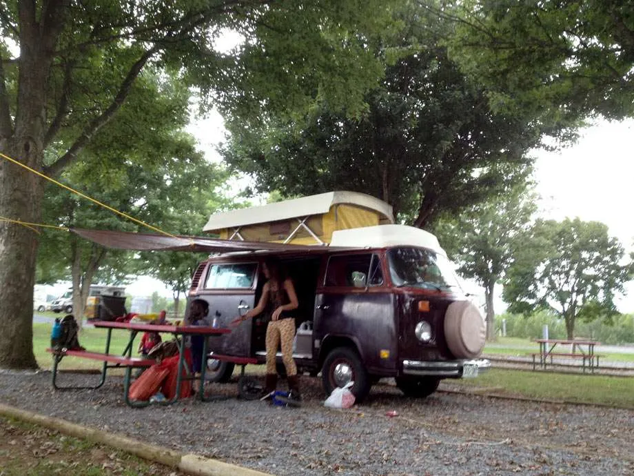 a woman and a child at a picnic table outside of a vw bus in a koa campground
