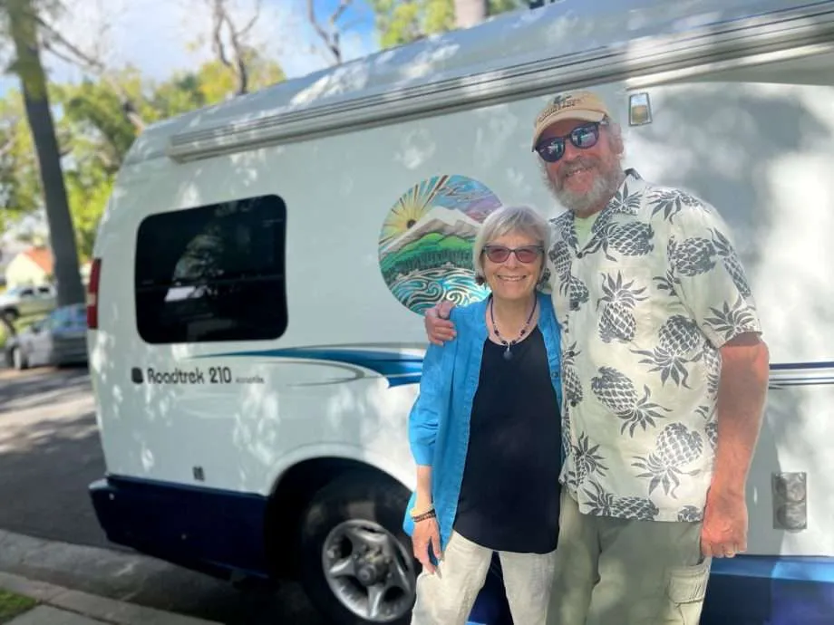 a retired couple (of hippies) standing in front of their Roadtrek campervan