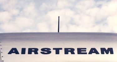 an Airstream logo, painted across the top of a just barely visible roof of one of these aluminum travel trailers, a cloudy blue sky in the background